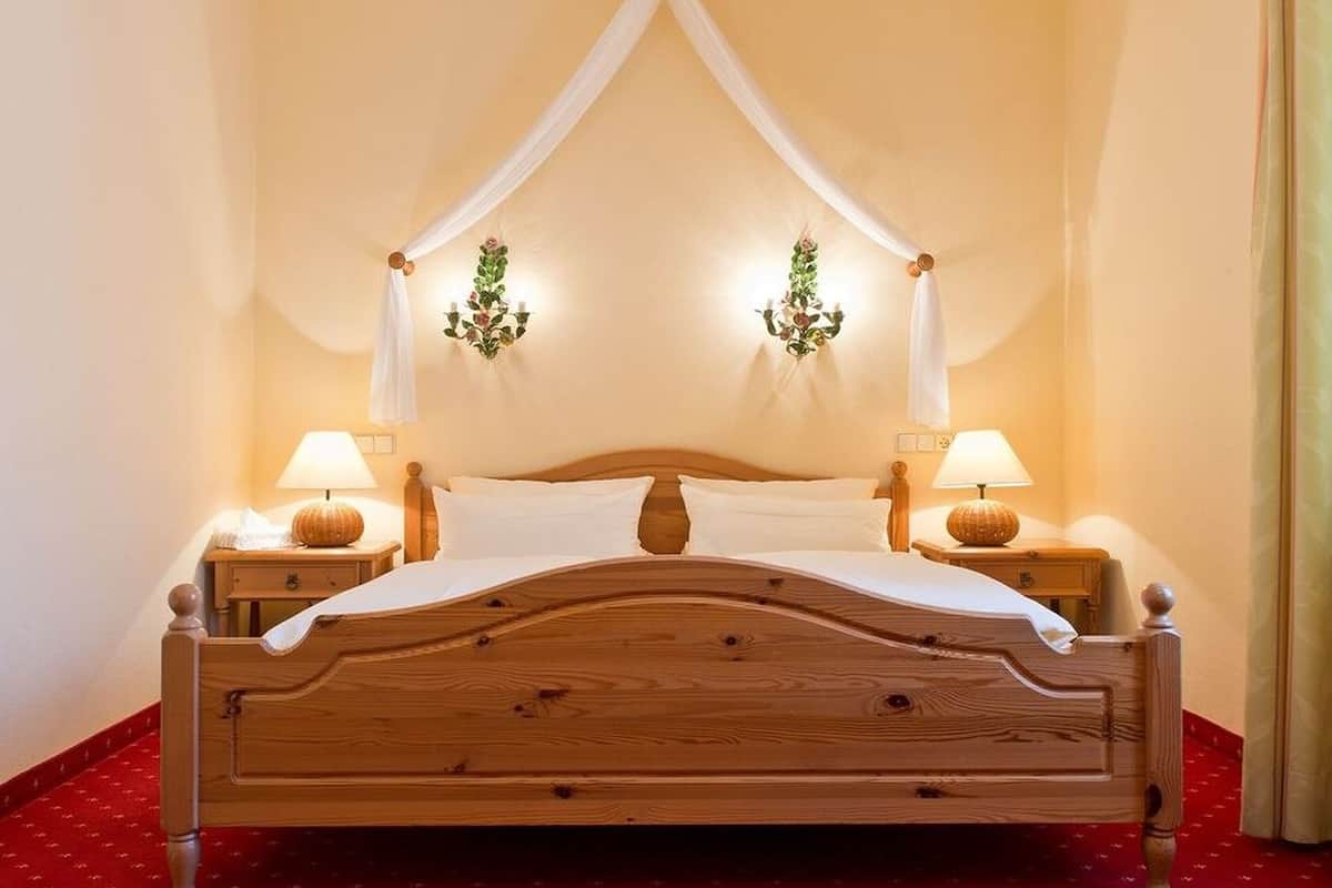 Una cama de madera con dosel, dos lámparas de noche y apliques de pared con diseños florales.