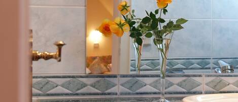 Un baño con encimera de mármol, un lavabo y un espejo que refleja una pared con azulejos.