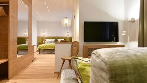Una habitación de hotel moderna con suelo de madera, un televisor de pantalla plana grande, una zona de comedor con mesa y sillas, y un rincón de descanso acogedor con un banco.
