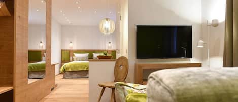 Una habitación de hotel moderna con suelo de madera, un televisor de pantalla plana grande, una zona de comedor con mesa y sillas, y un rincón de descanso acogedor con un banco.