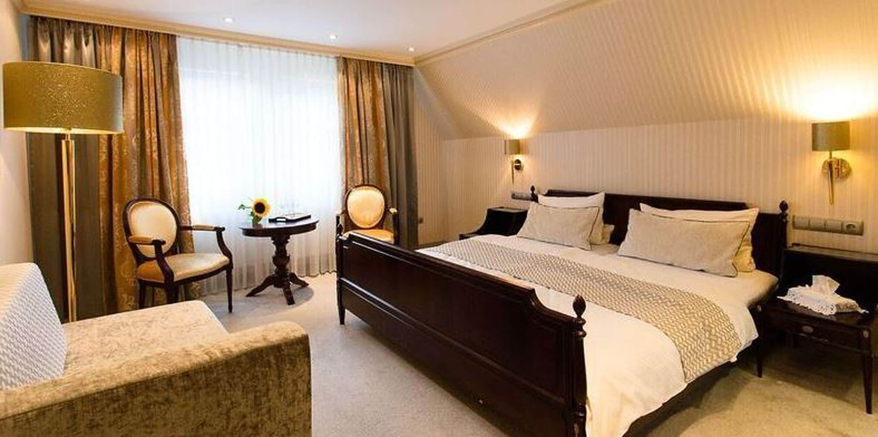 A hotel room with a large bed, a chair, a small table, and a lamp.