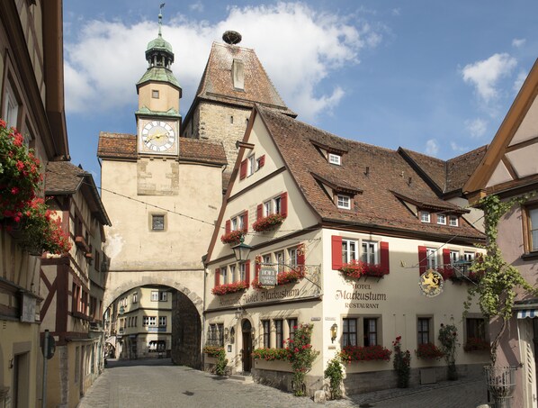 A historic building with a clock tower, red shutters, and flower boxes. - Romantik Hotel Markusturm (Rothenburg ob der Tauber)