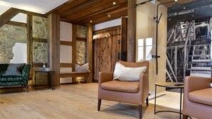 Habitación con piso de madera, pared de piedra y un ventanal grande. Se observan dos sillones de cuero, una mesita y un banco.