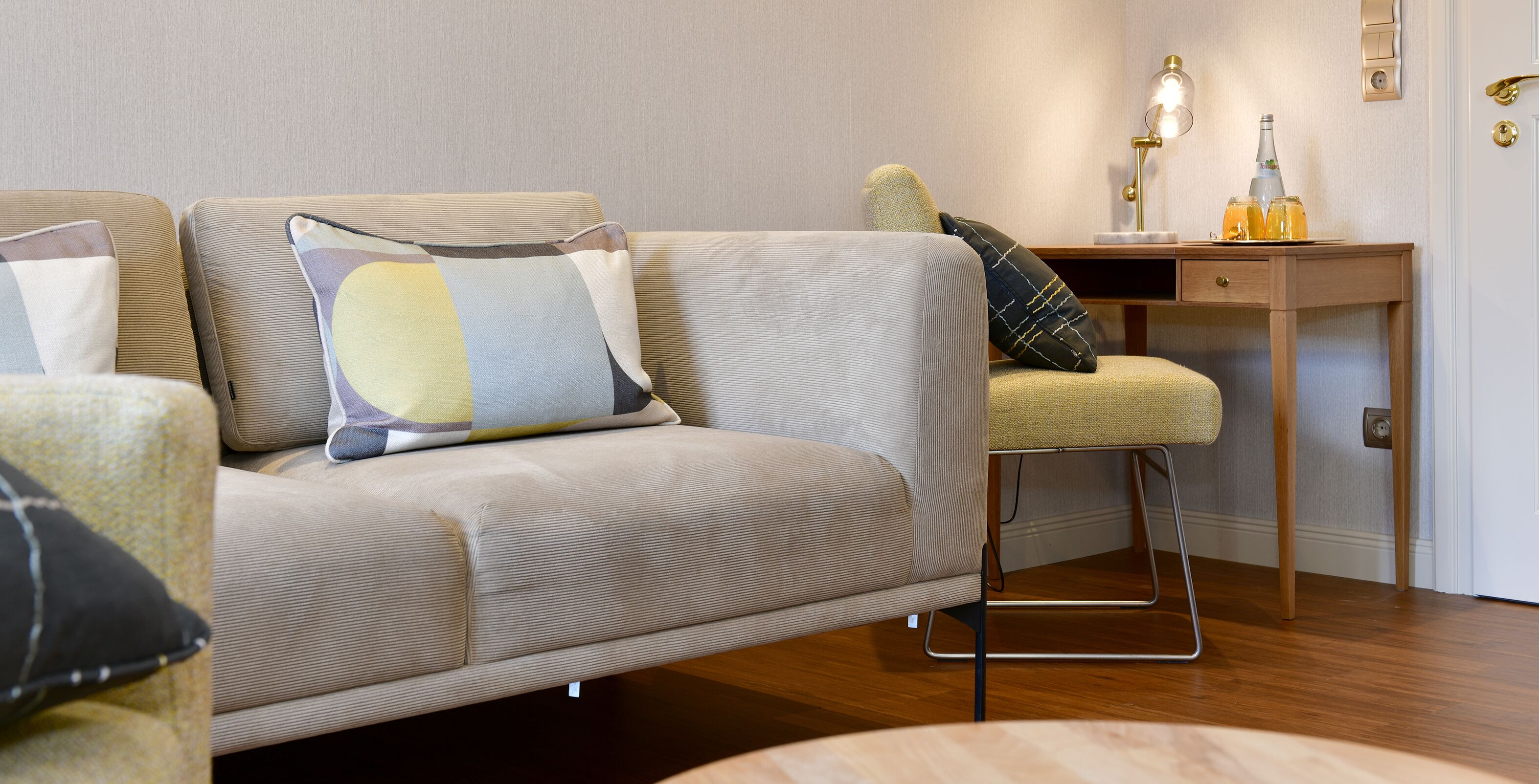 A modern living room with a sofa, armchair, and a small wooden table with a lamp and drinks.
