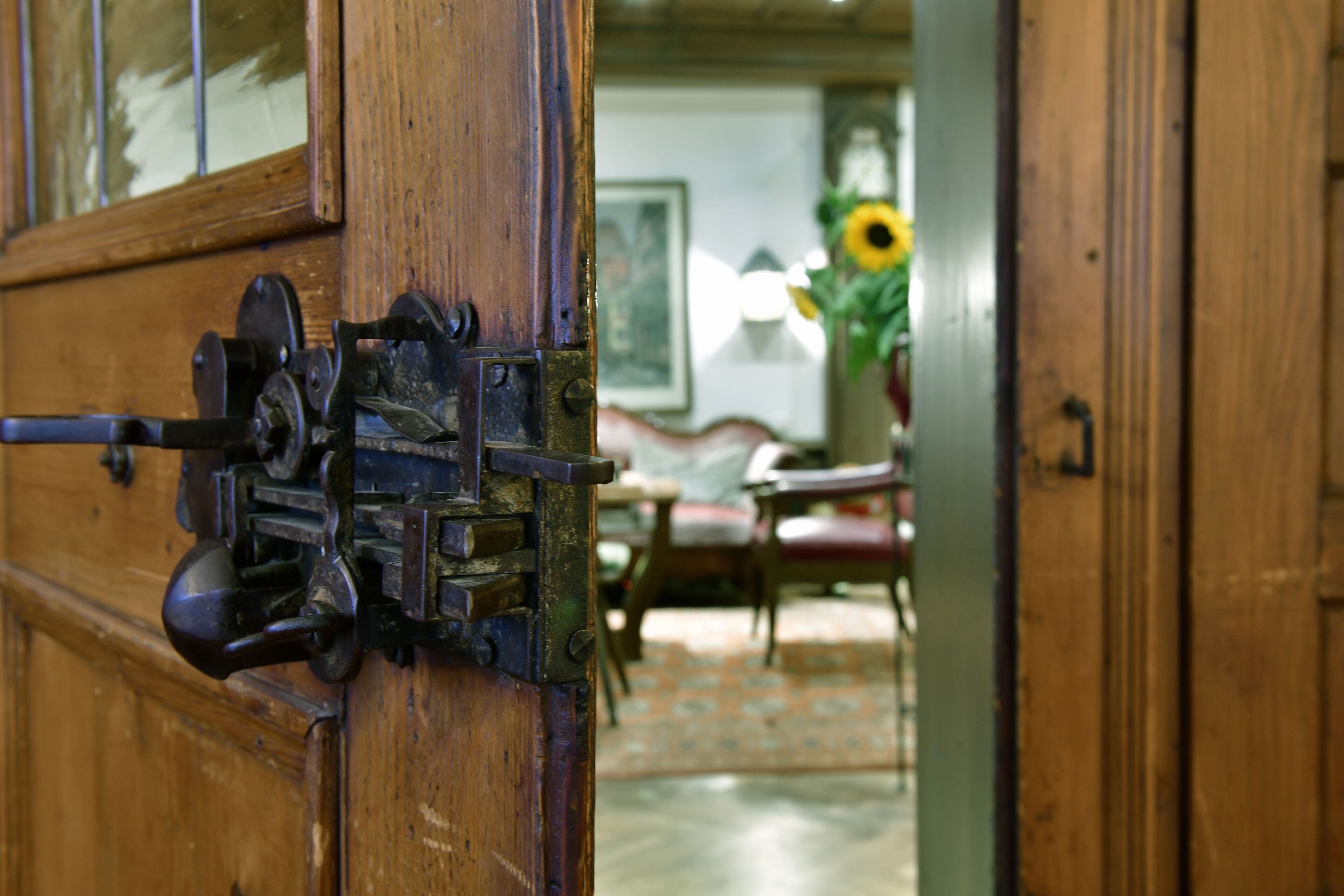 Una puerta de madera con un pestillo metálico y una ventana que da a una habitación con un sofá, una mesa y un florero con flores.