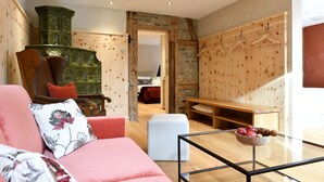 Una sala de estar moderna con un sofá, un reposapiés y una mesa de centro de vidrio. Hay un banco de madera y un armario de madera con perchas.
