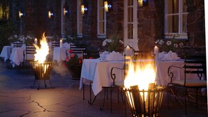 Een terras met eettafels, omringd door stenen muren en verlicht met lantaarns.