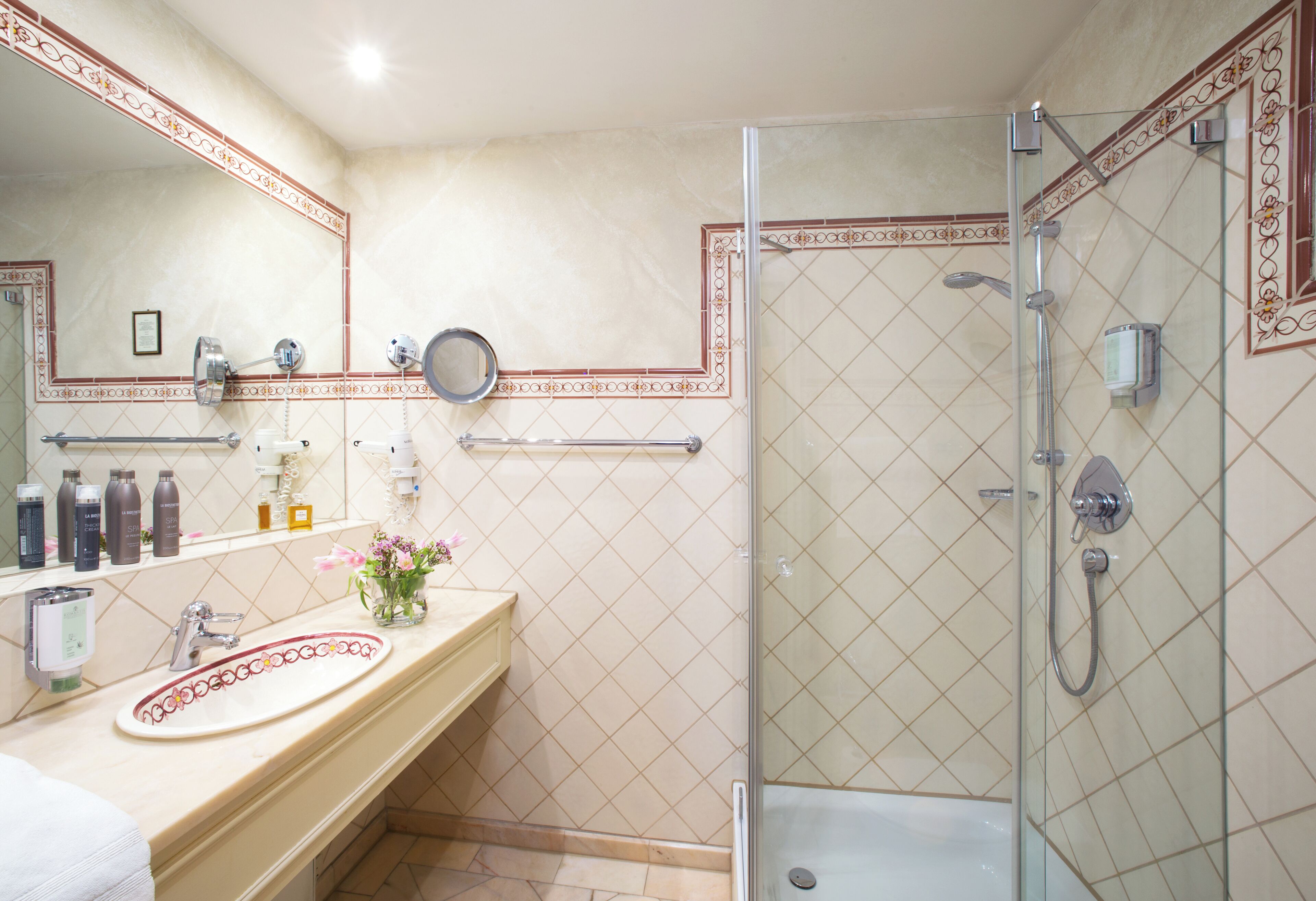 A bathroom with a sink, mirror, shower, and decorative tiles.