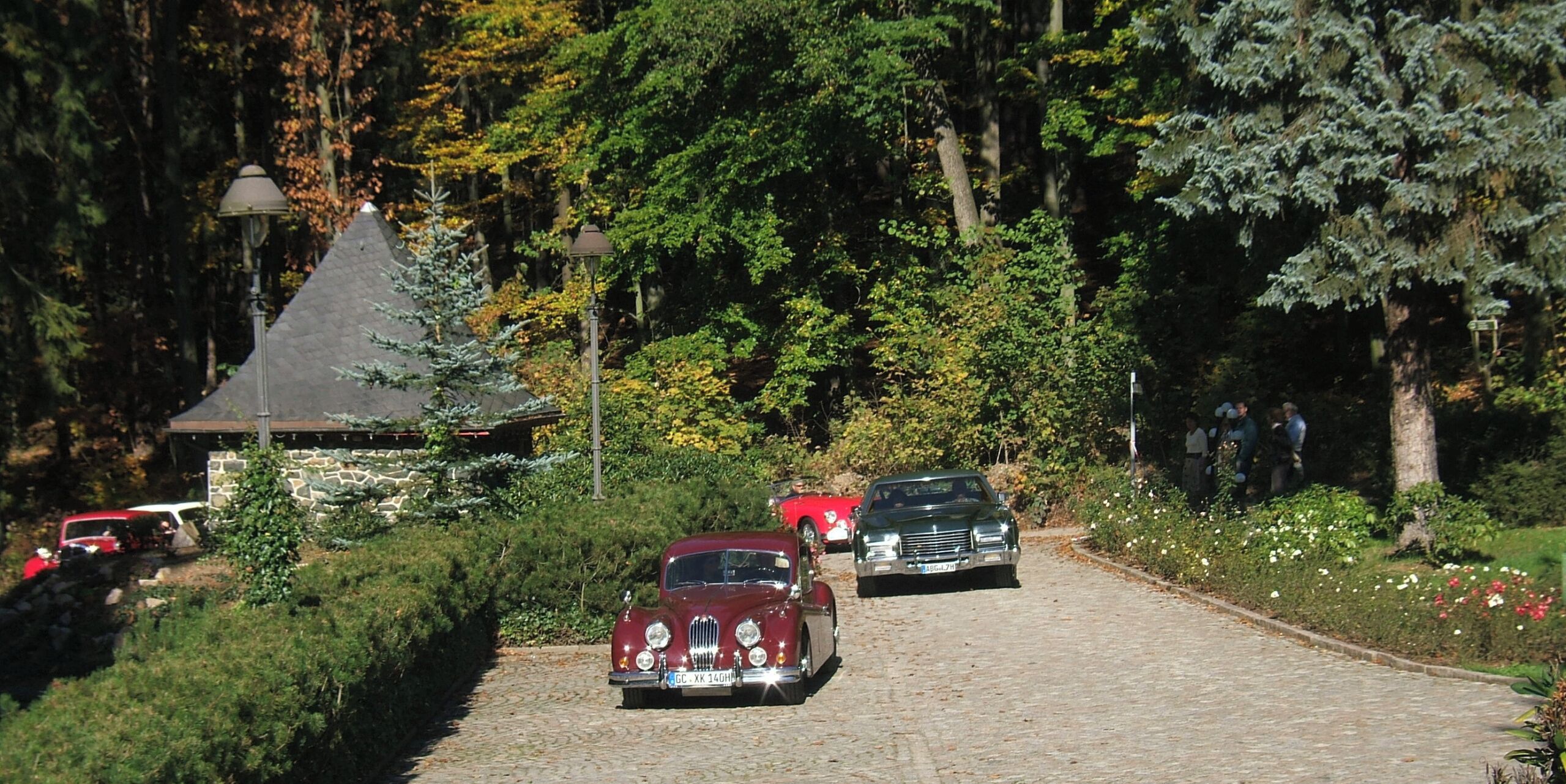 A cobblestone path with vintage cars parked on the side.