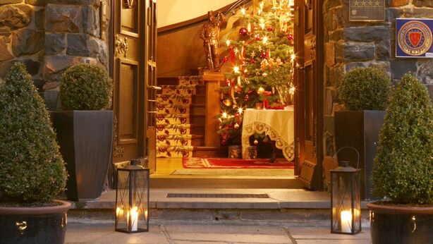 Een hotelgevel van steen, een kerstkrans en een verlichte kerstboom.
