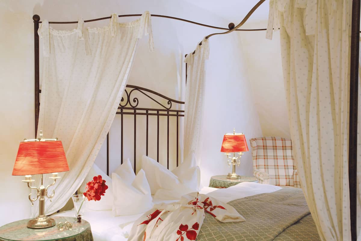 Een hemelbed met witte lakens, twee bedlampen en een sprei met bloemenprint.