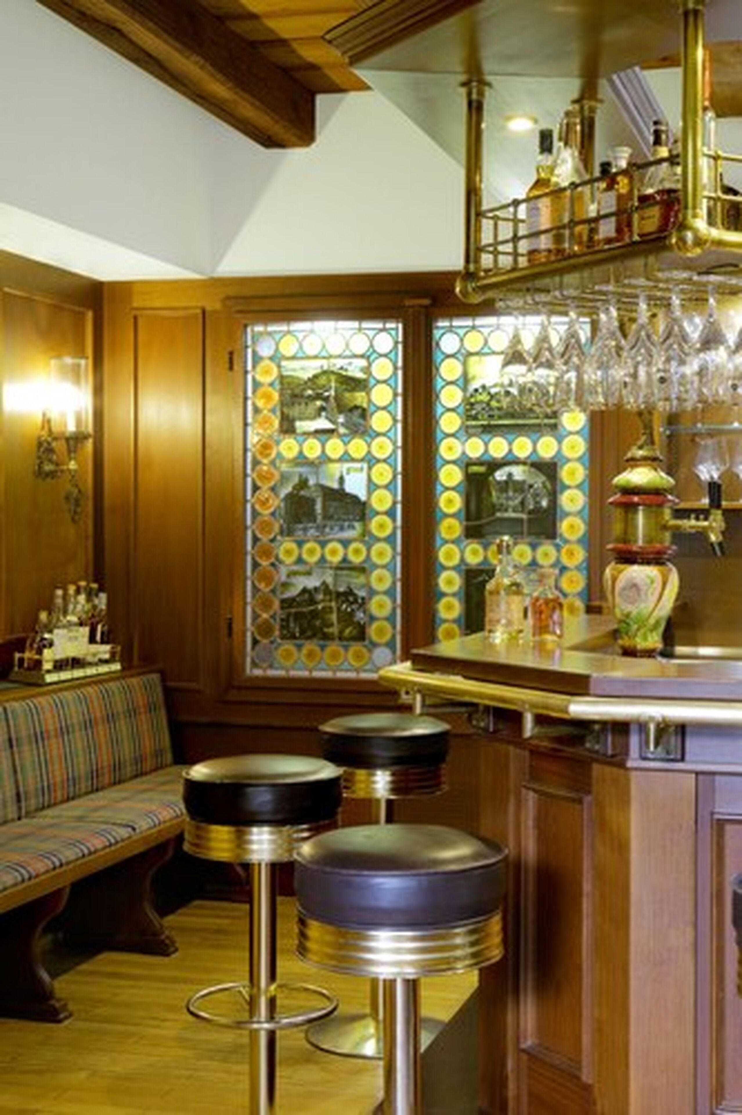 A bar area with wooden paneling, a stained glass window, and bar stools.