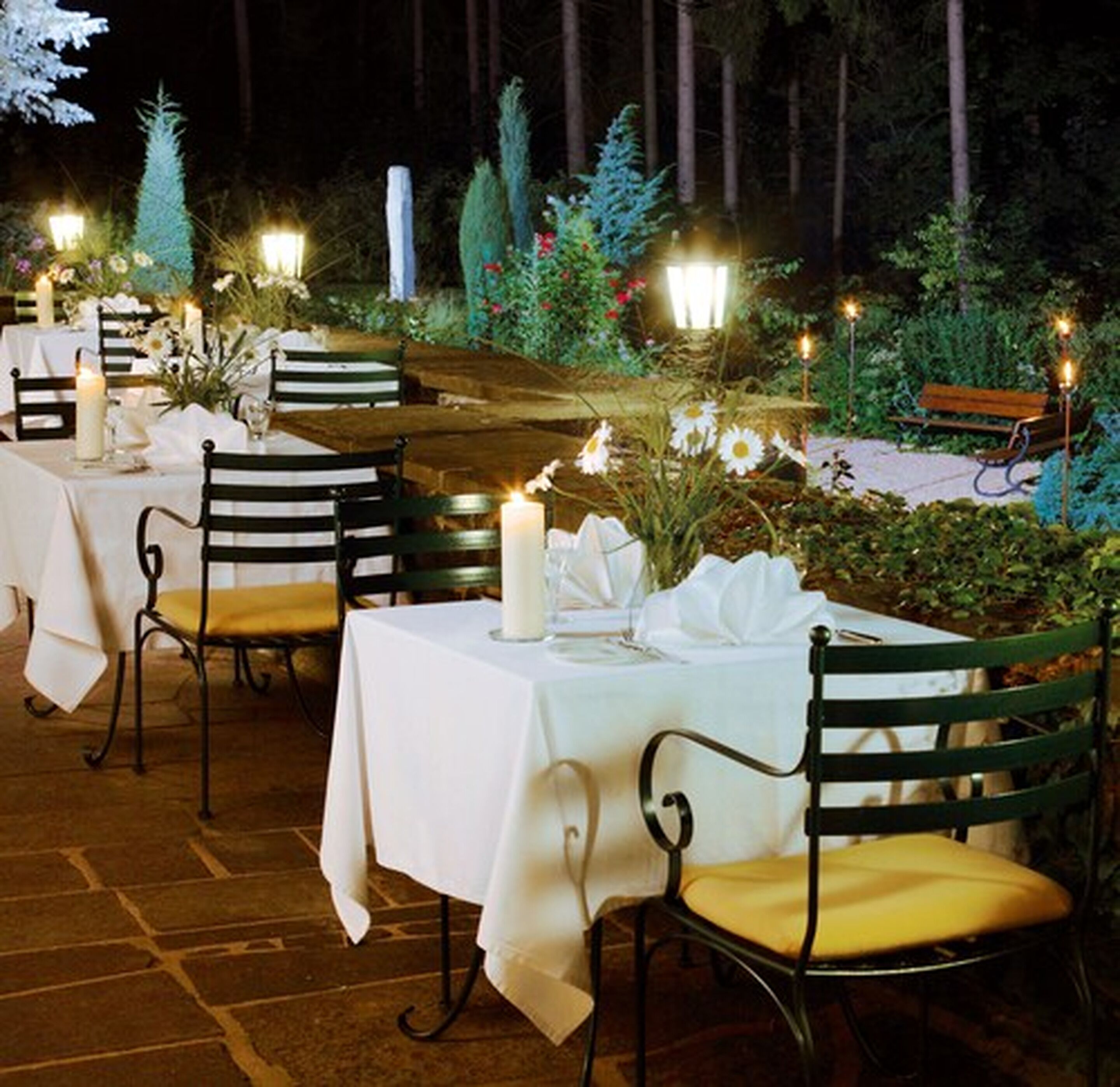 An outdoor dining area with tables and chairs, candles, and decorative lights.