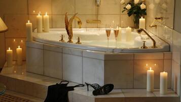Ein luxuriöses Badezimmer mit einer freistehenden Badewanne, mehreren beleuchteten Kerzen, einem goldenen Dekorationsstück und einer Vase mit weißen Rosen.
