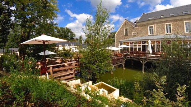 Een rivierlandschap met terras, een houten brug en een gebouw met een stenen gevel.