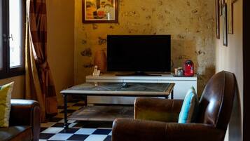 A cozy room with a checkered floor, a flat-screen TV, a coffee machine, and a sofa with cushions.