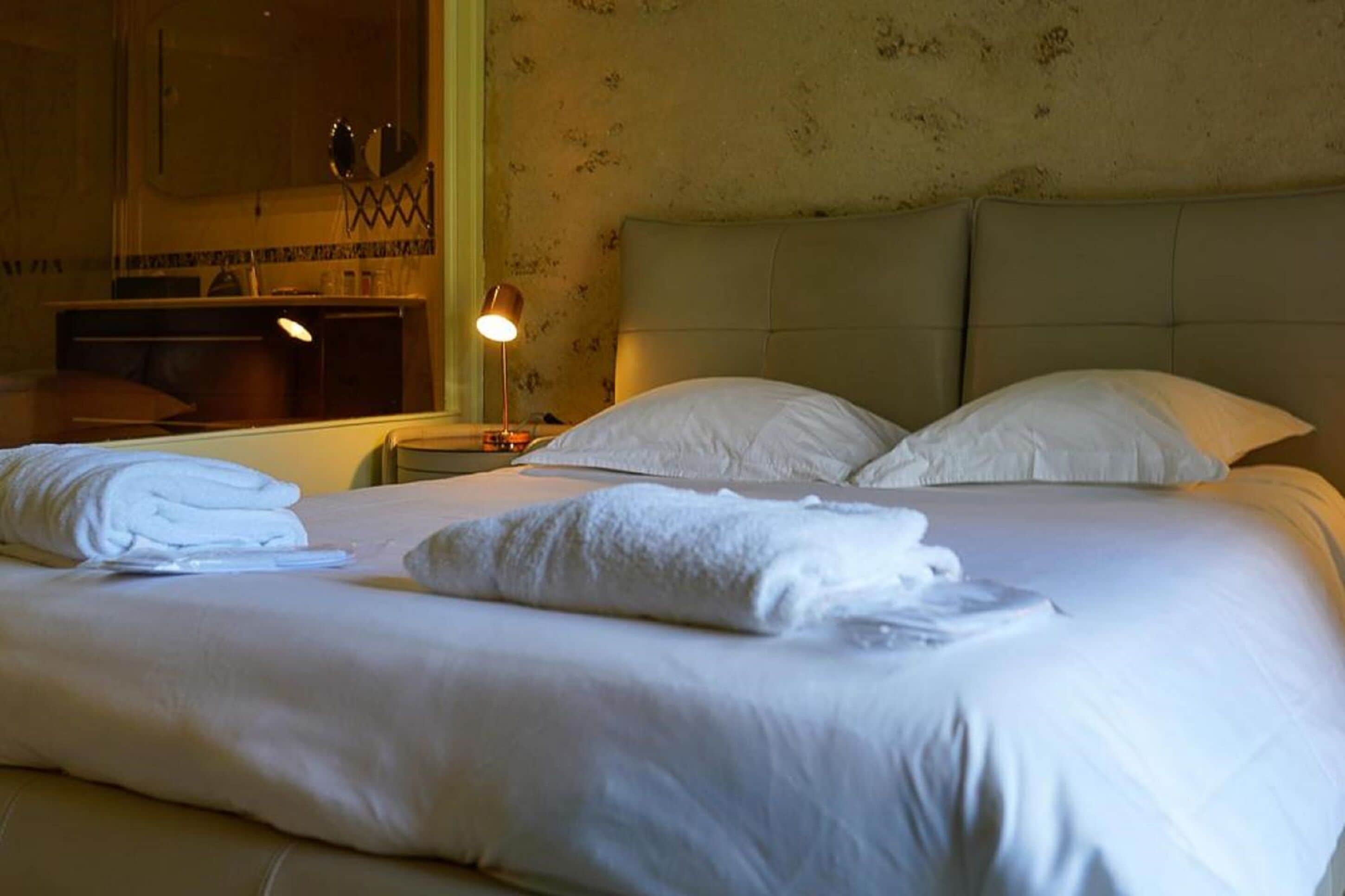 A neatly made bed with white linens and pillows, a bedside lamp, and a mirror on the wall.