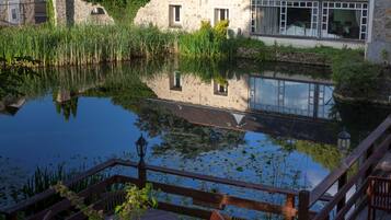 A serene riverside view with a wooden deck, stone buildings, and a clear reflection in the water.