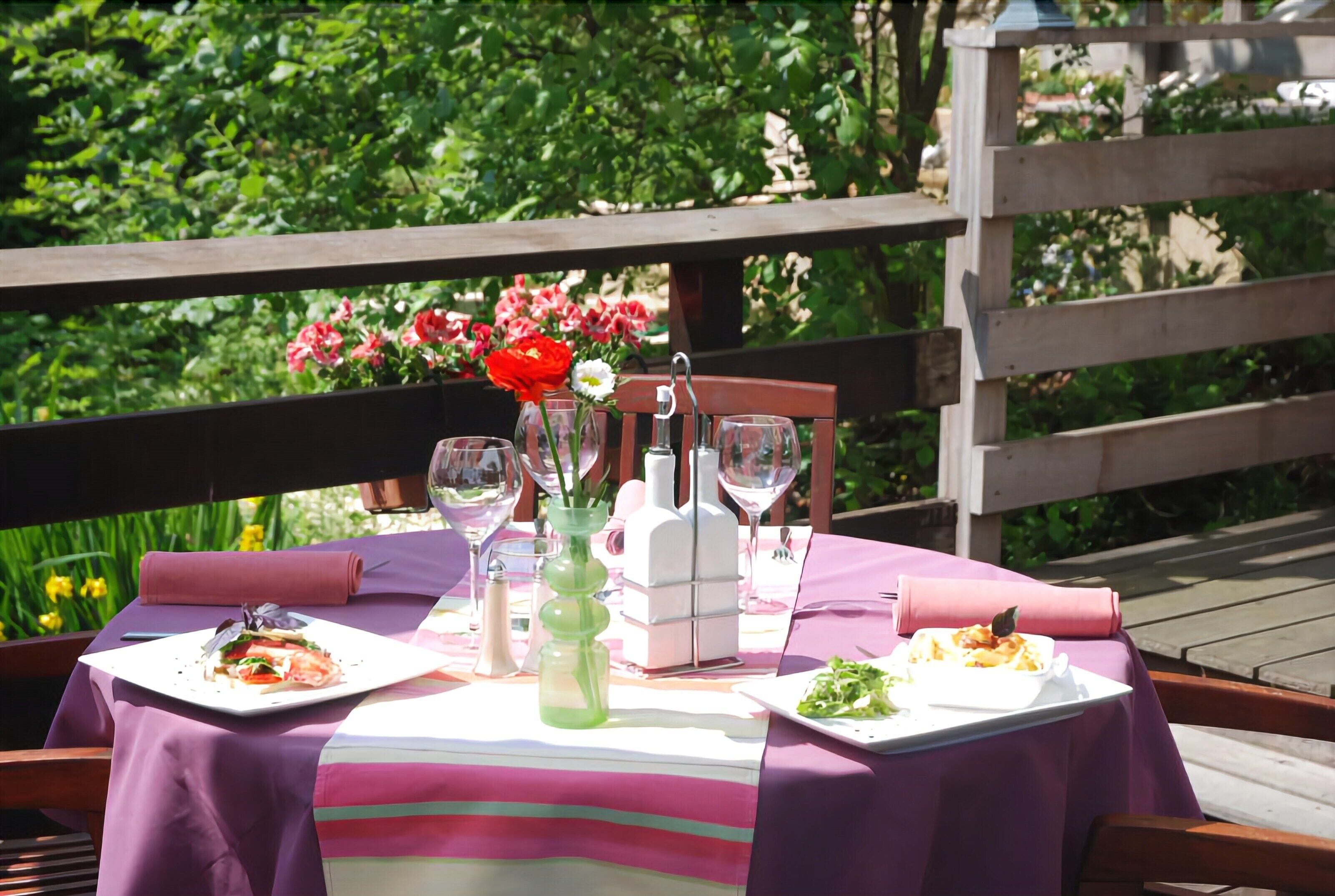 Een terras met een eettafel voor twee personen, compleet met borden eten, wijn glazen en een decoratieve vaas.