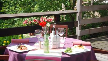Een terras met een eettafel voor twee personen, compleet met borden eten, wijn glazen en een decoratieve vaas.