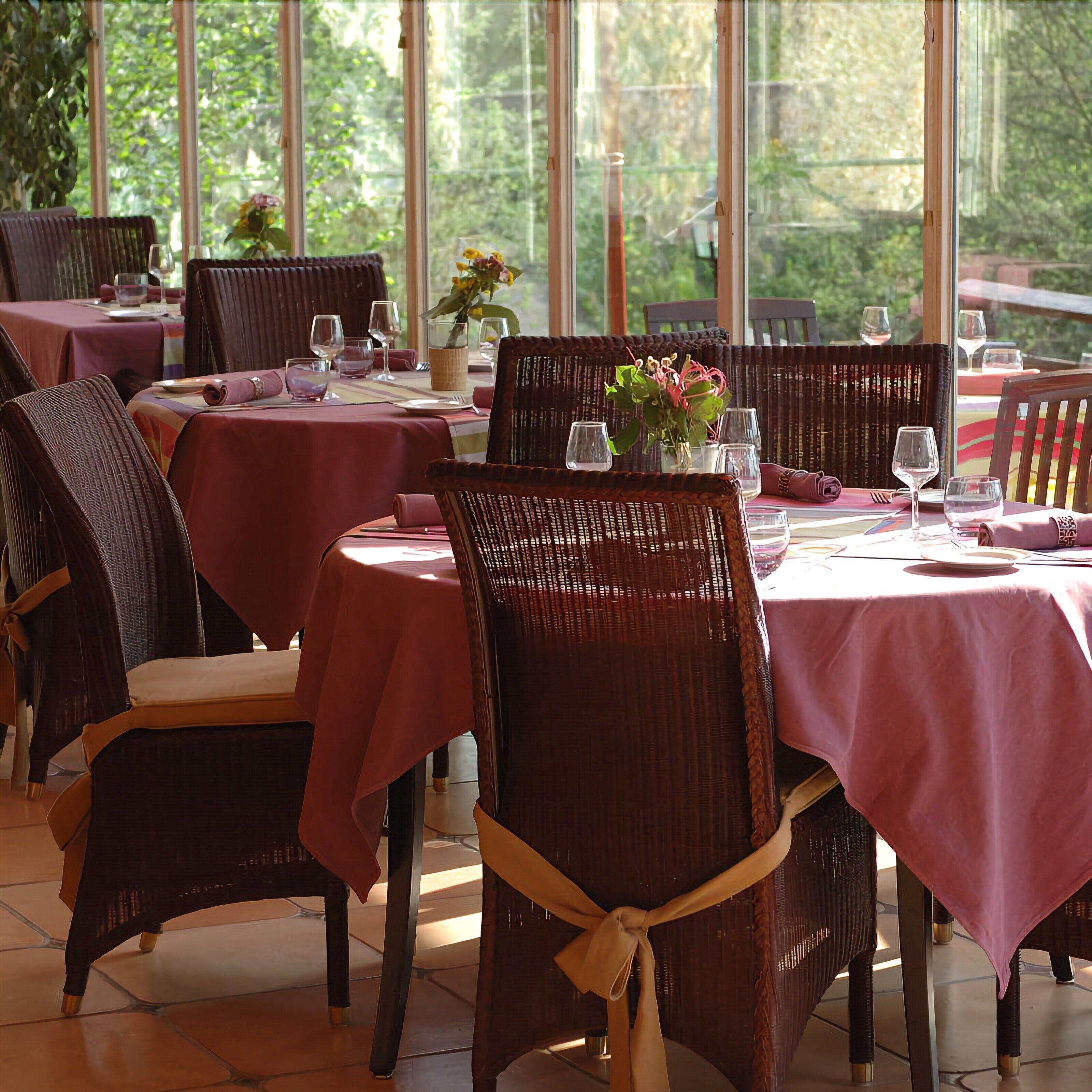 A restaurant with multiple tables and wicker chairs, each set with wine glasses and cutlery.