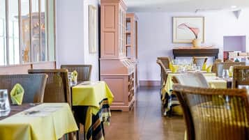 Um restaurante com várias mesas, cadeiras de vime e uma janela grande.
