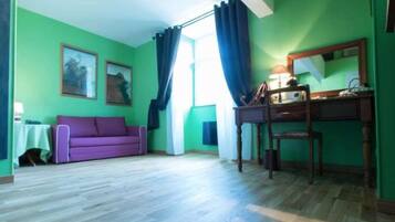 Una habitación con sofá morado, escritorio de madera, espejo y ventana con cortinas.