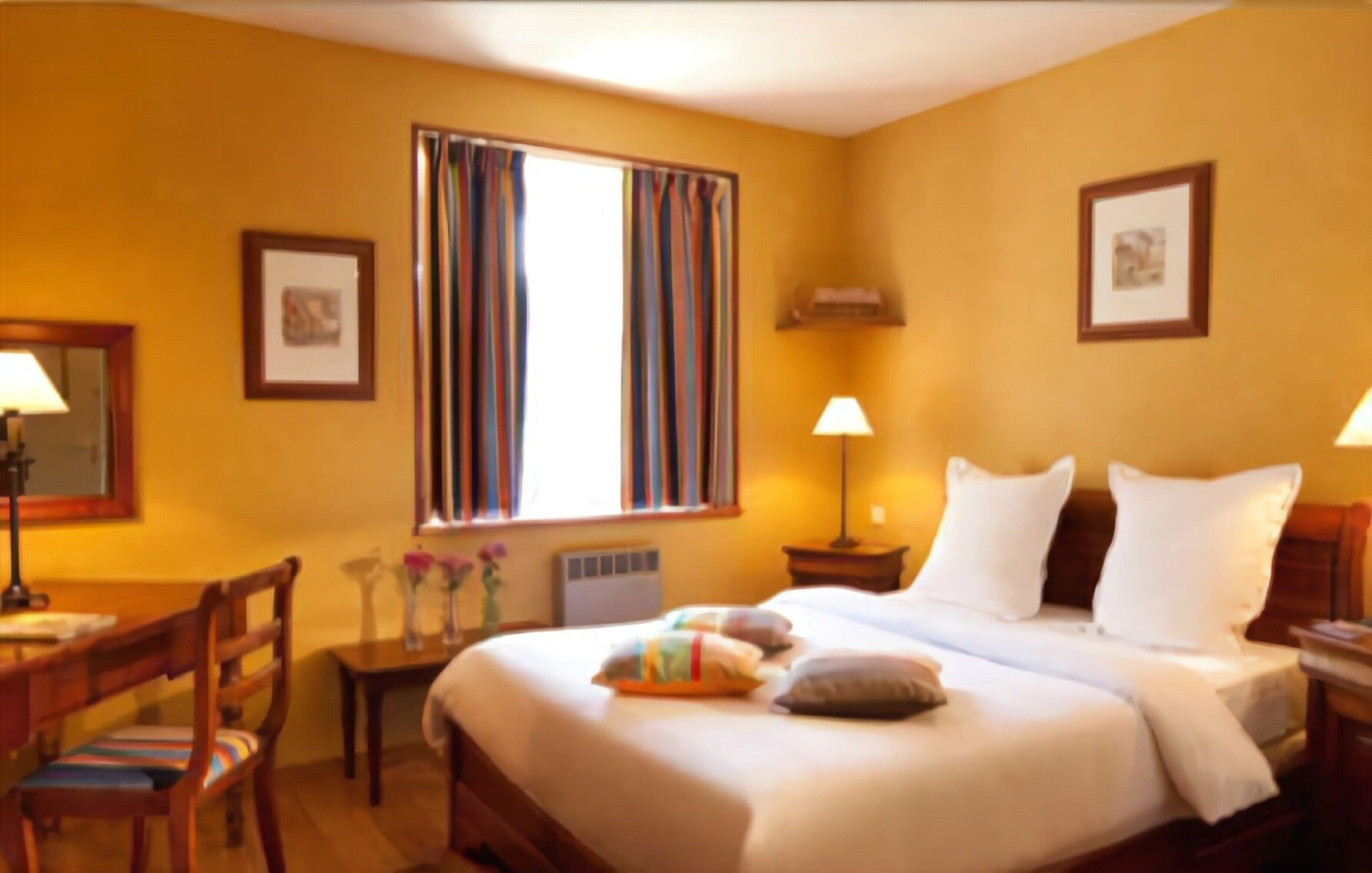 A hotel room with a large bed, two bedside tables, a chair, a desk, and a window with curtains.