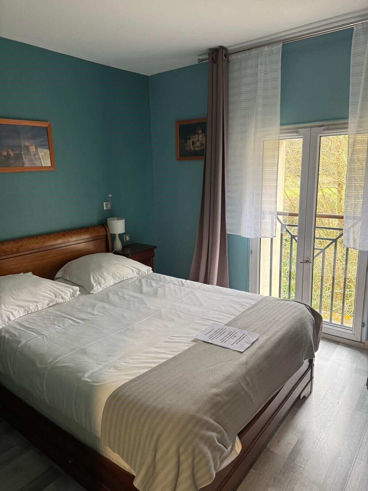 Et soveværelse med seng, et natbord, en lampe, et vindue med gardiner og en balkon.