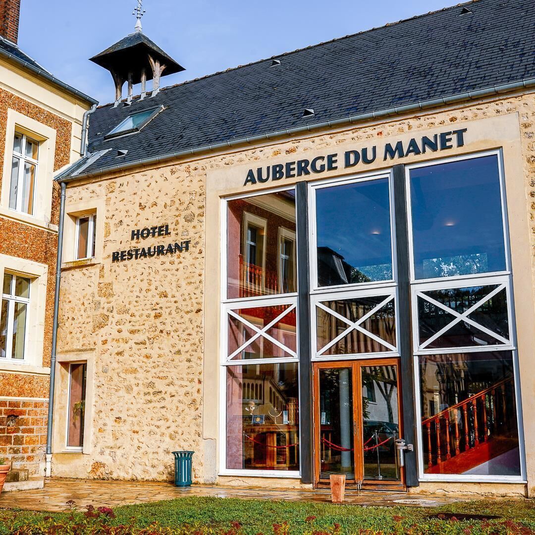 Ein Gebäude mit der Aufschrift "AUBERGE DU MANET HOTEL RESTAURANT", große Fenster und eine Treppe zum Eingang.