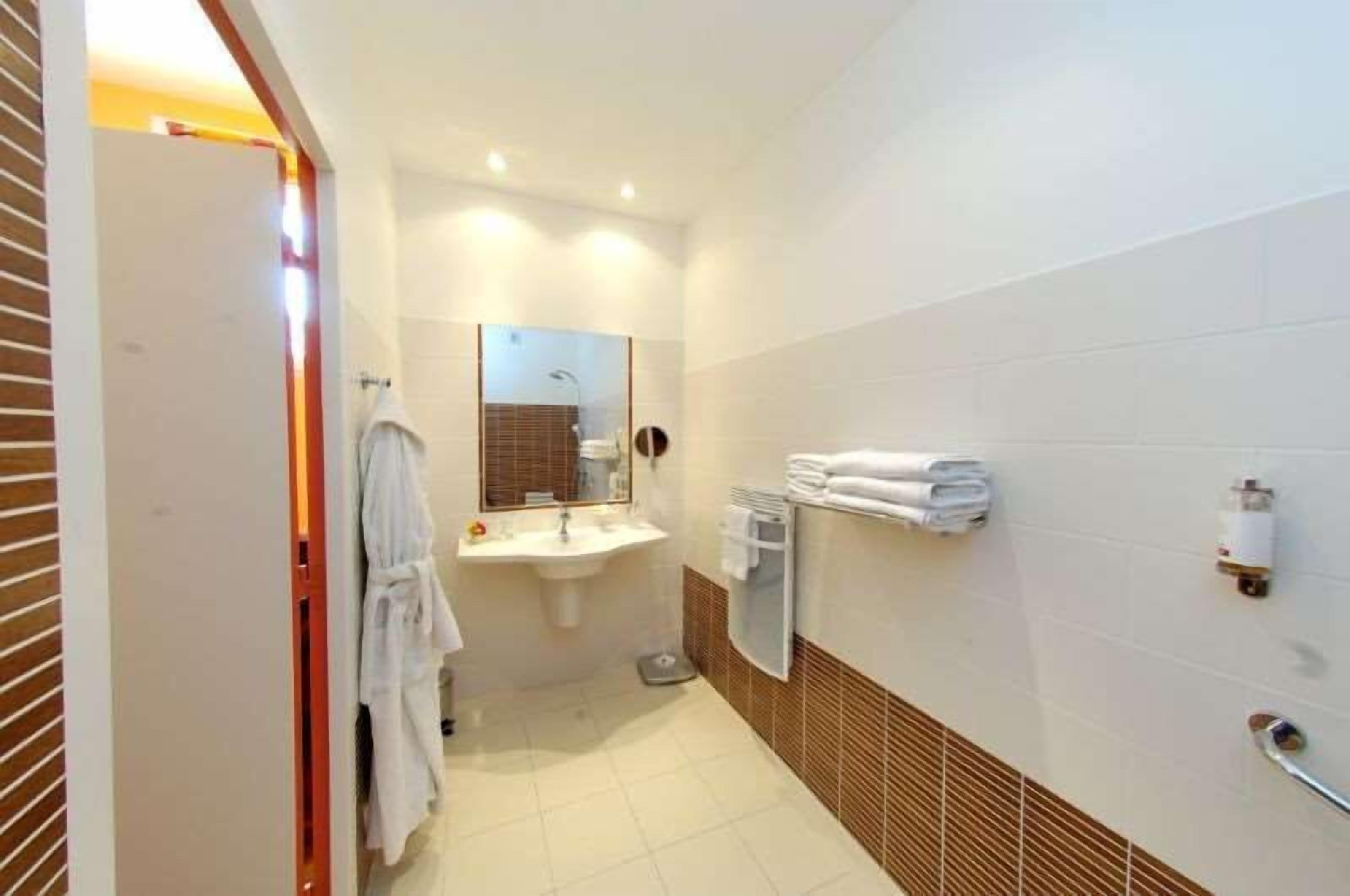 Baño de hotel con lavamanos, espejo, toallero y balanza.