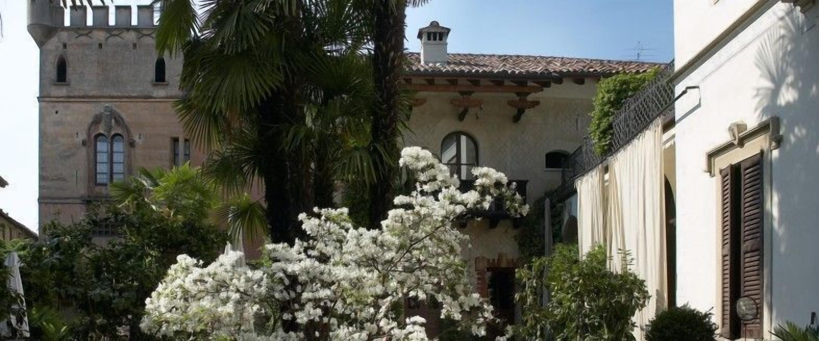 Un edificio histórico con una torre, rodeado de exuberante follaje y árboles con flores blancas.