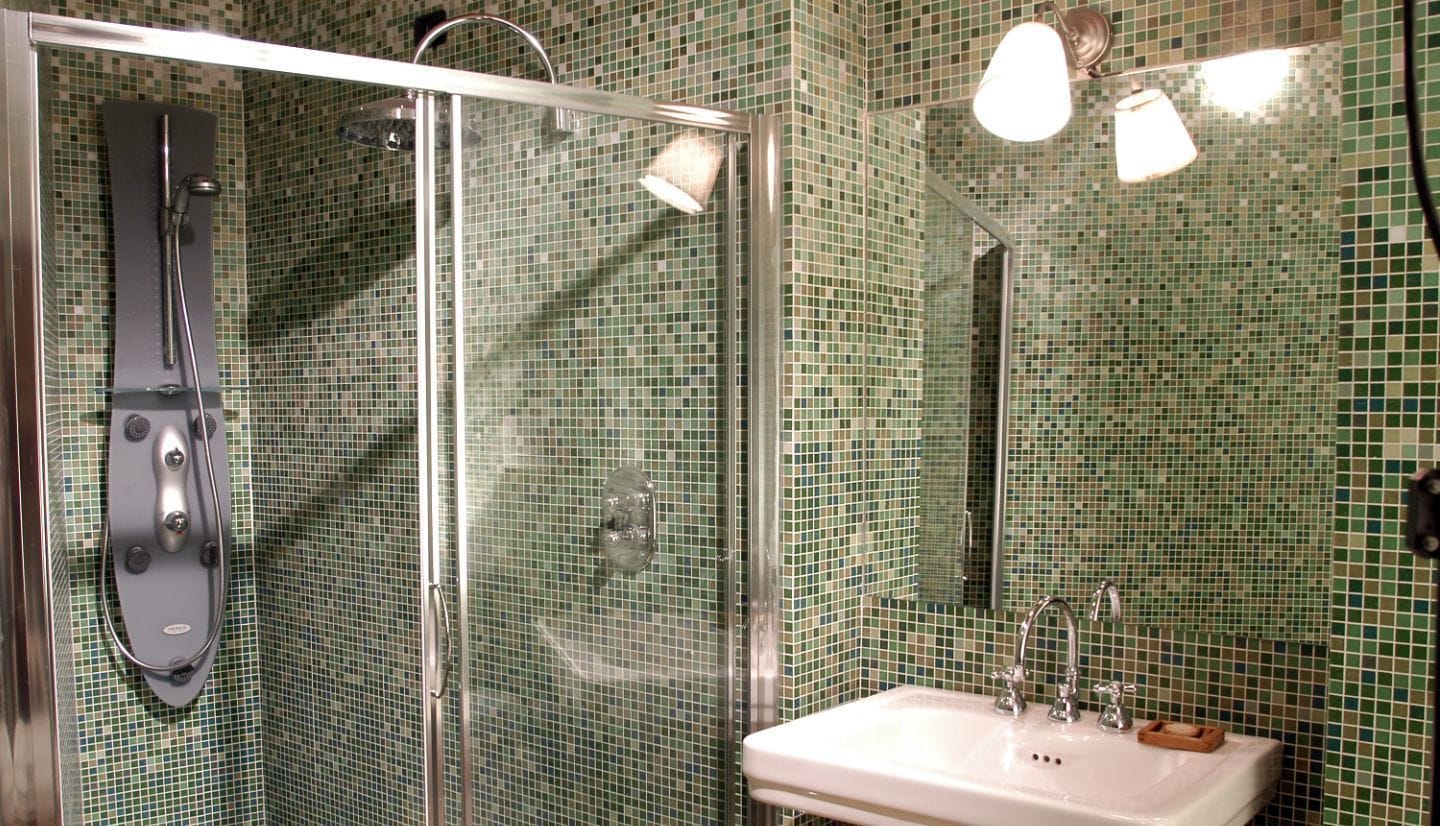 Un baño con ducha de vidrio, lavamanos con espejo y paredes de mosaicos.