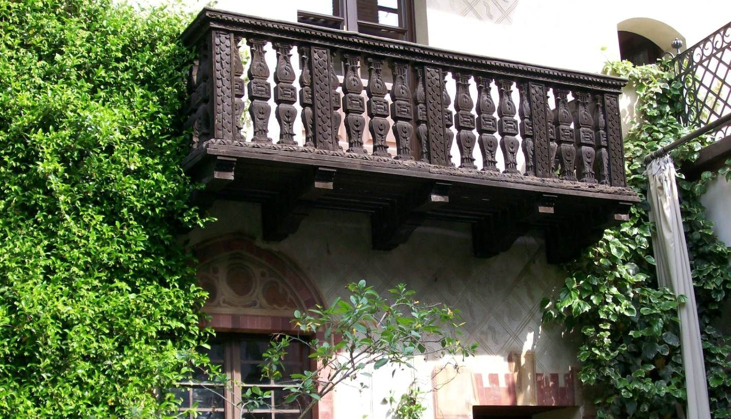 Un balcón con barandillas metálicas detalladas y fachada de edificio parcialmente cubierta de follaje verde.