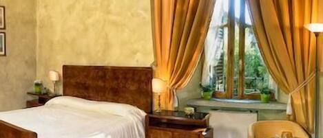 A bedroom with a bed, a nightstand, a lamp, a window with curtains, and a small table with a chair.
