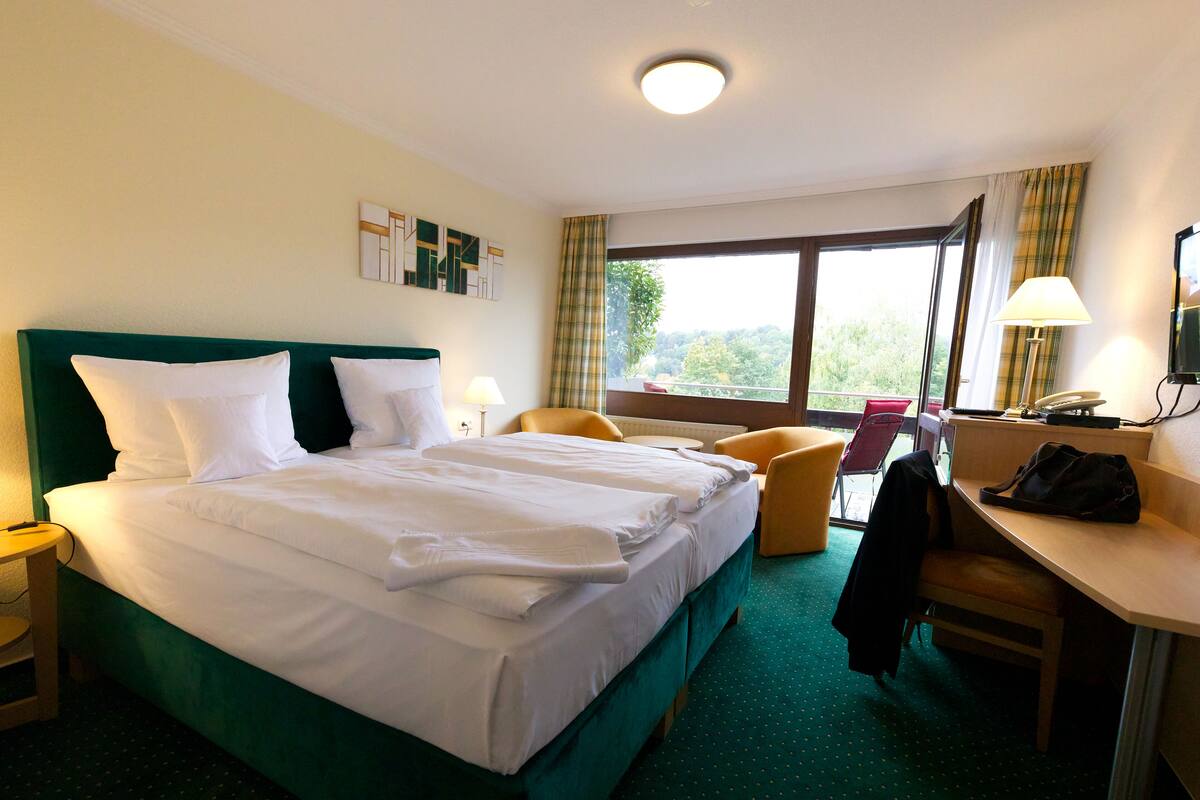 Une chambre d’hôtel avec un grand lit, un bureau, une chaise et une vue sur l’extérieur.