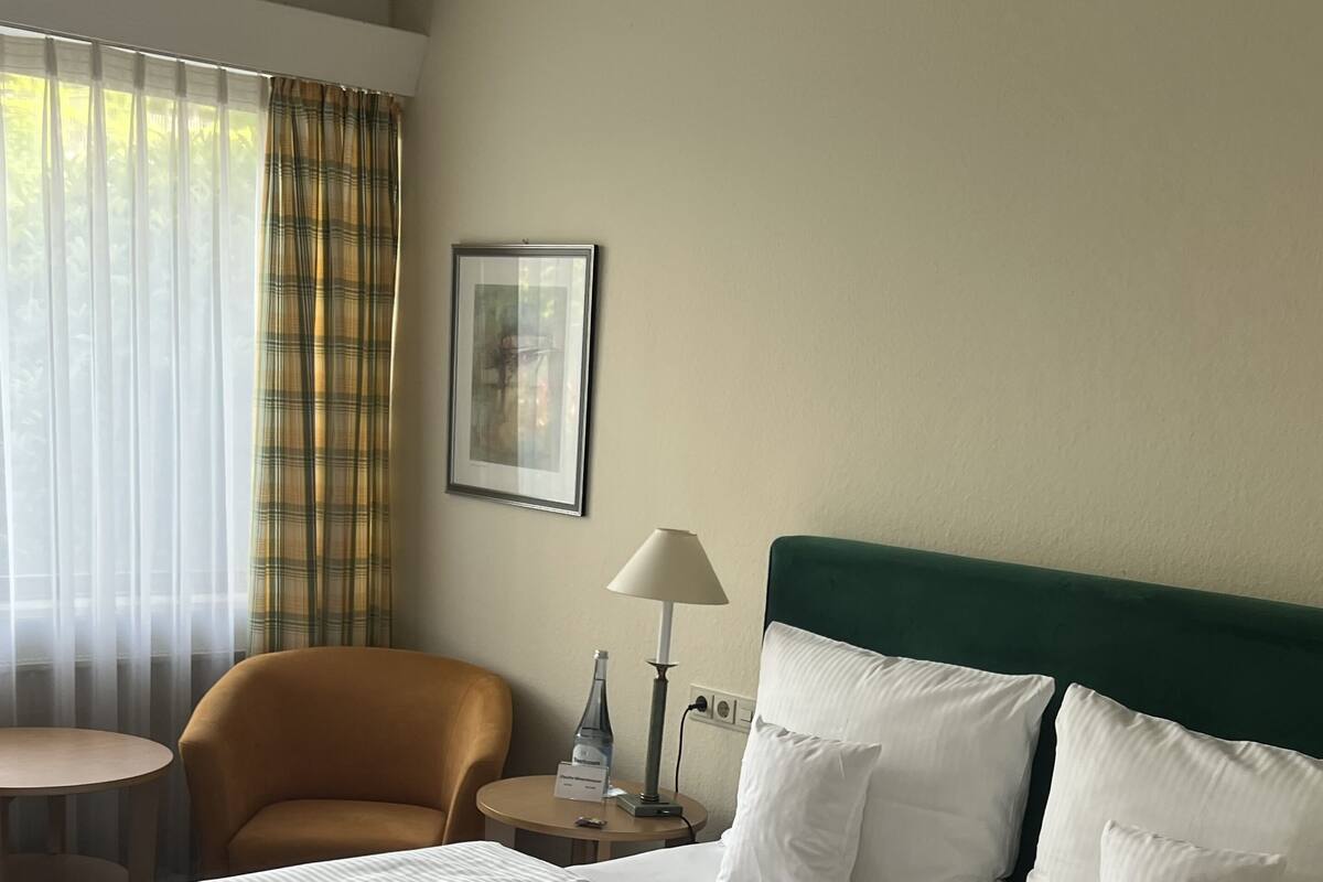 Une chambre d’hôtel avec un grand lit, une chaise, une petite table, une lampe et un tableau au mur.