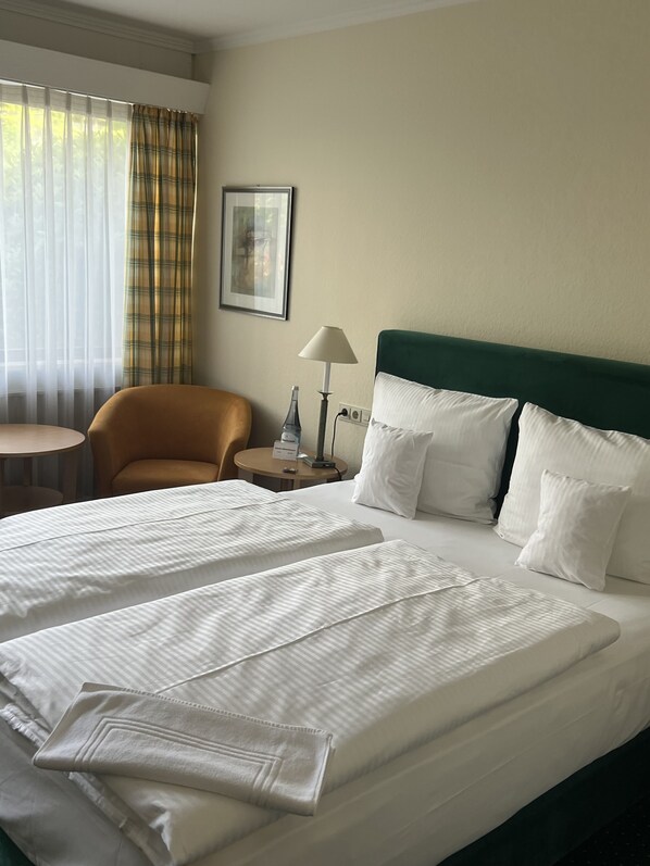 A hotel room with a large bed, a chair, a small table, a lamp, and a painting on the wall. - Parkhotel Hammerberg (Stolberg)