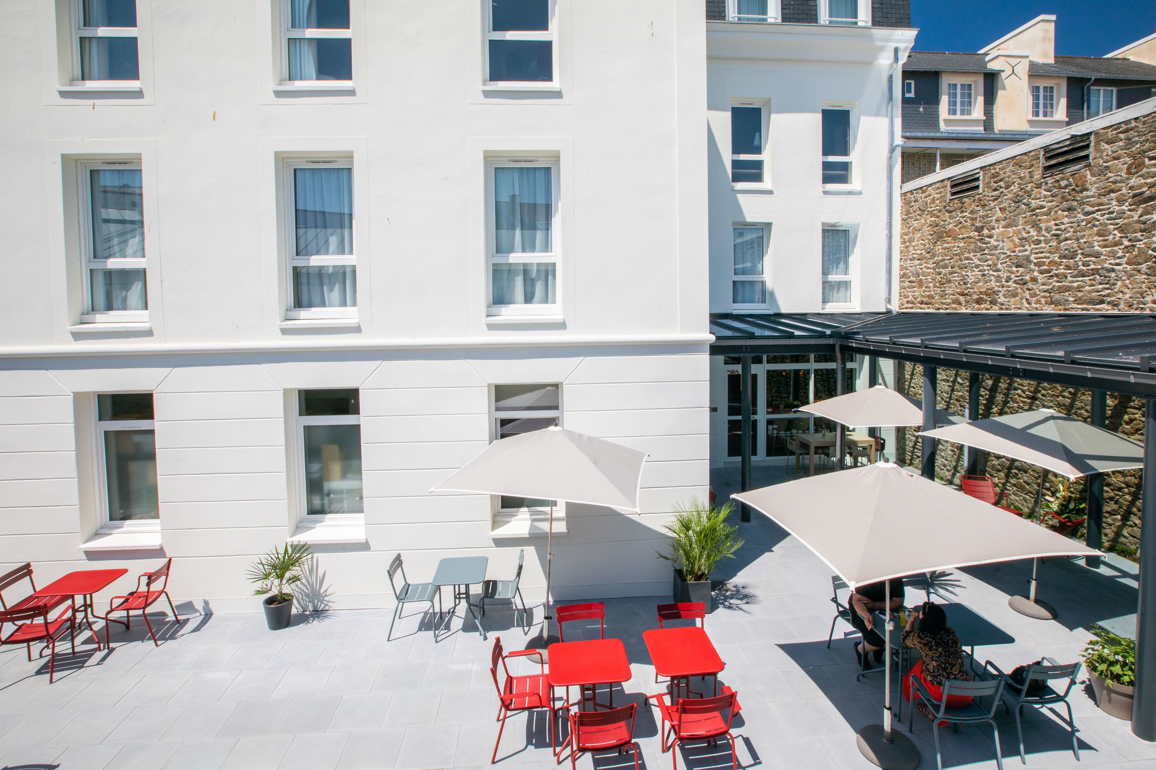 A hotel courtyard with outdoor seating, potted plants, and a stone wall.