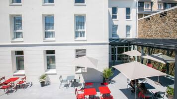 A hotel courtyard with outdoor seating, potted plants, and a stone wall.