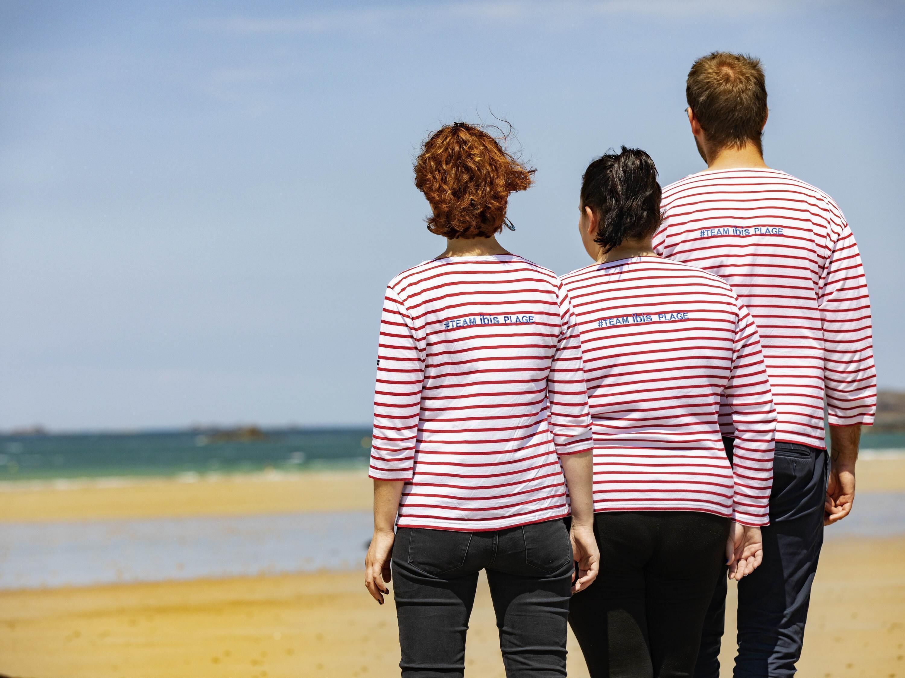 Three people walking on a beach wearing matching striped shirts.