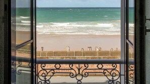 Une vue sur une plage, prise à travers une fenêtre ornée d’une rambarde en métal.