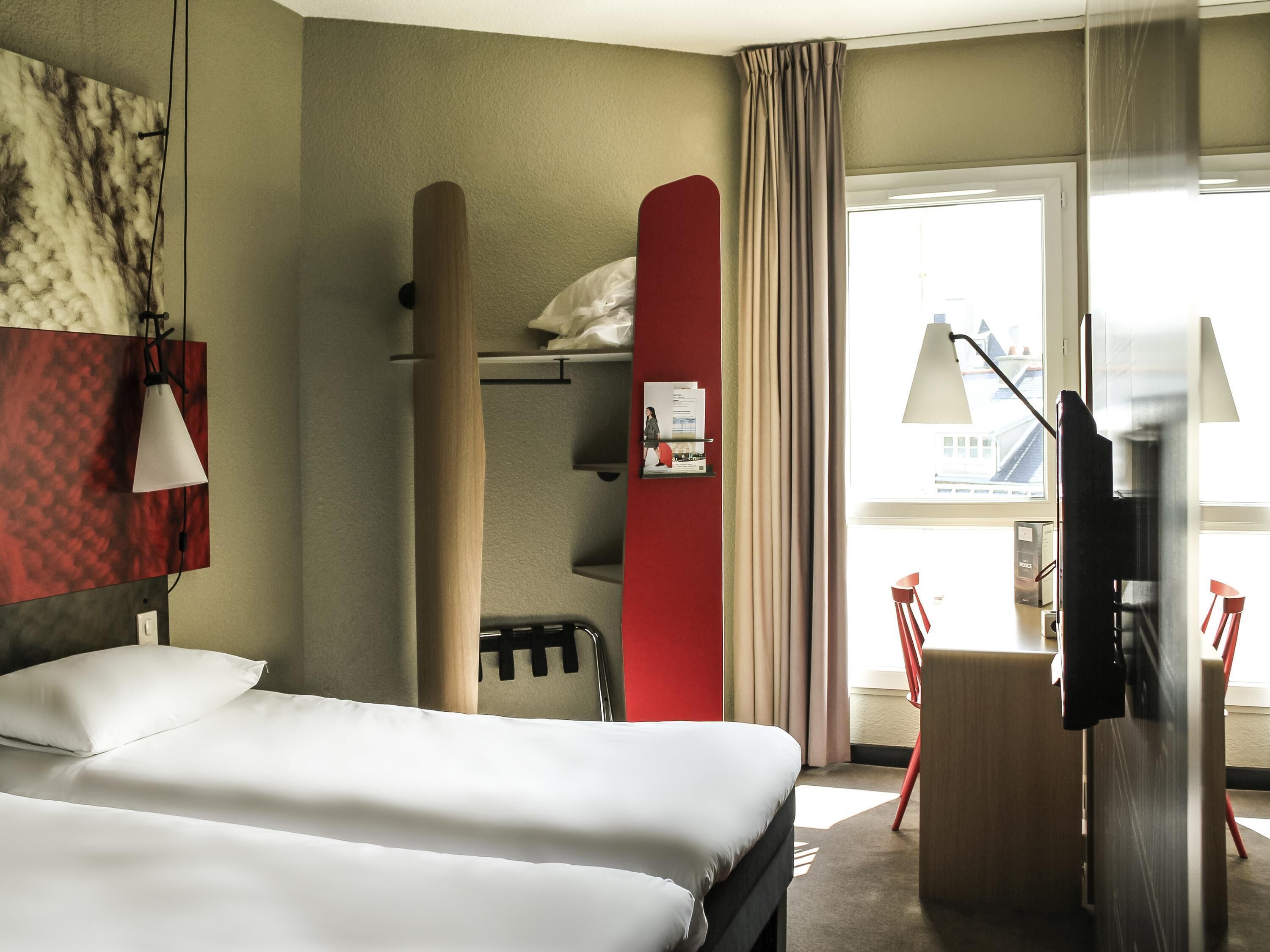 Una habitación de hotel con cama, escritorio, televisión y ventana con vistas.