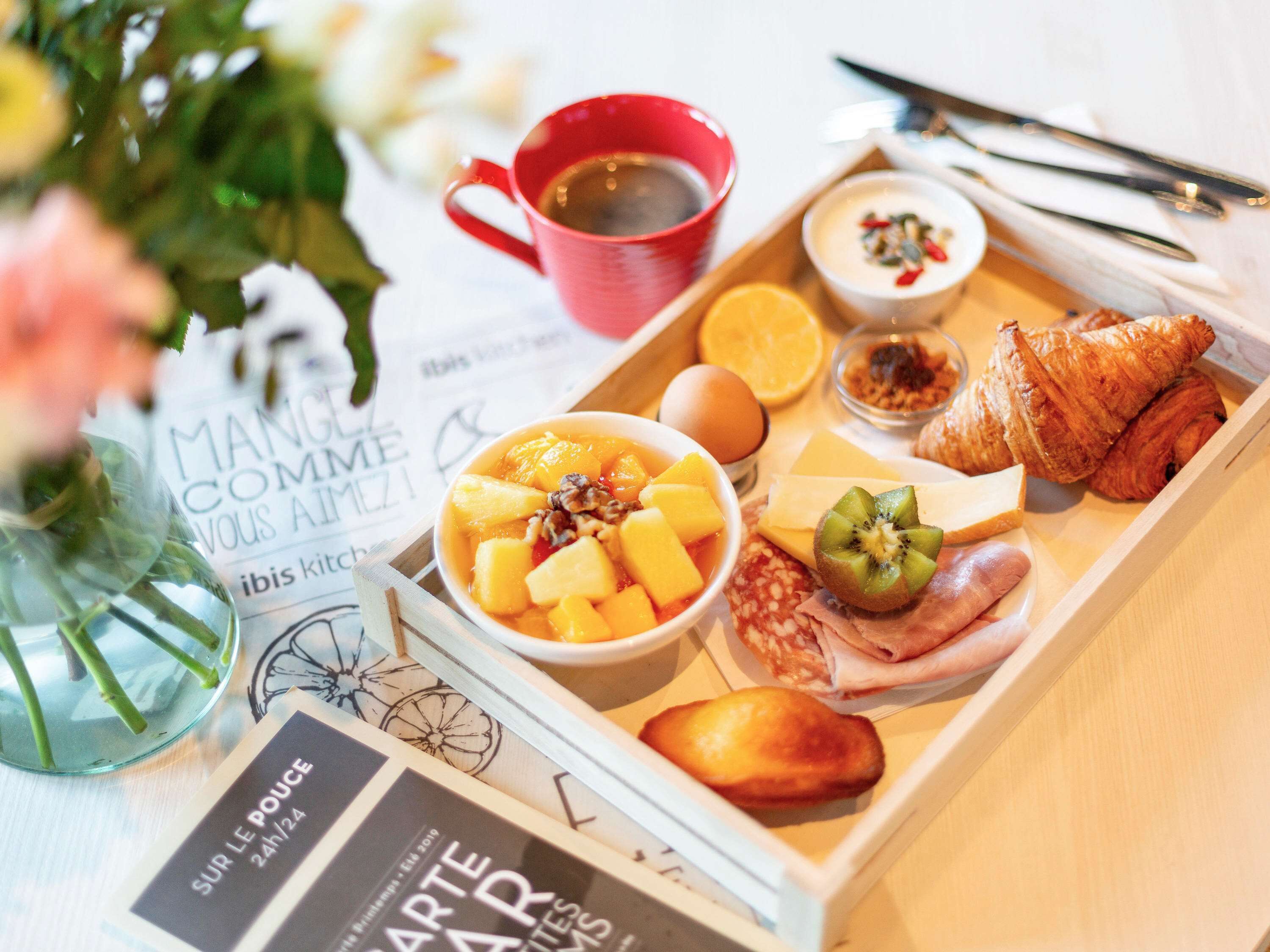 Una bandeja con alimentos, entre ellos frutas, un croissant y una bebida.