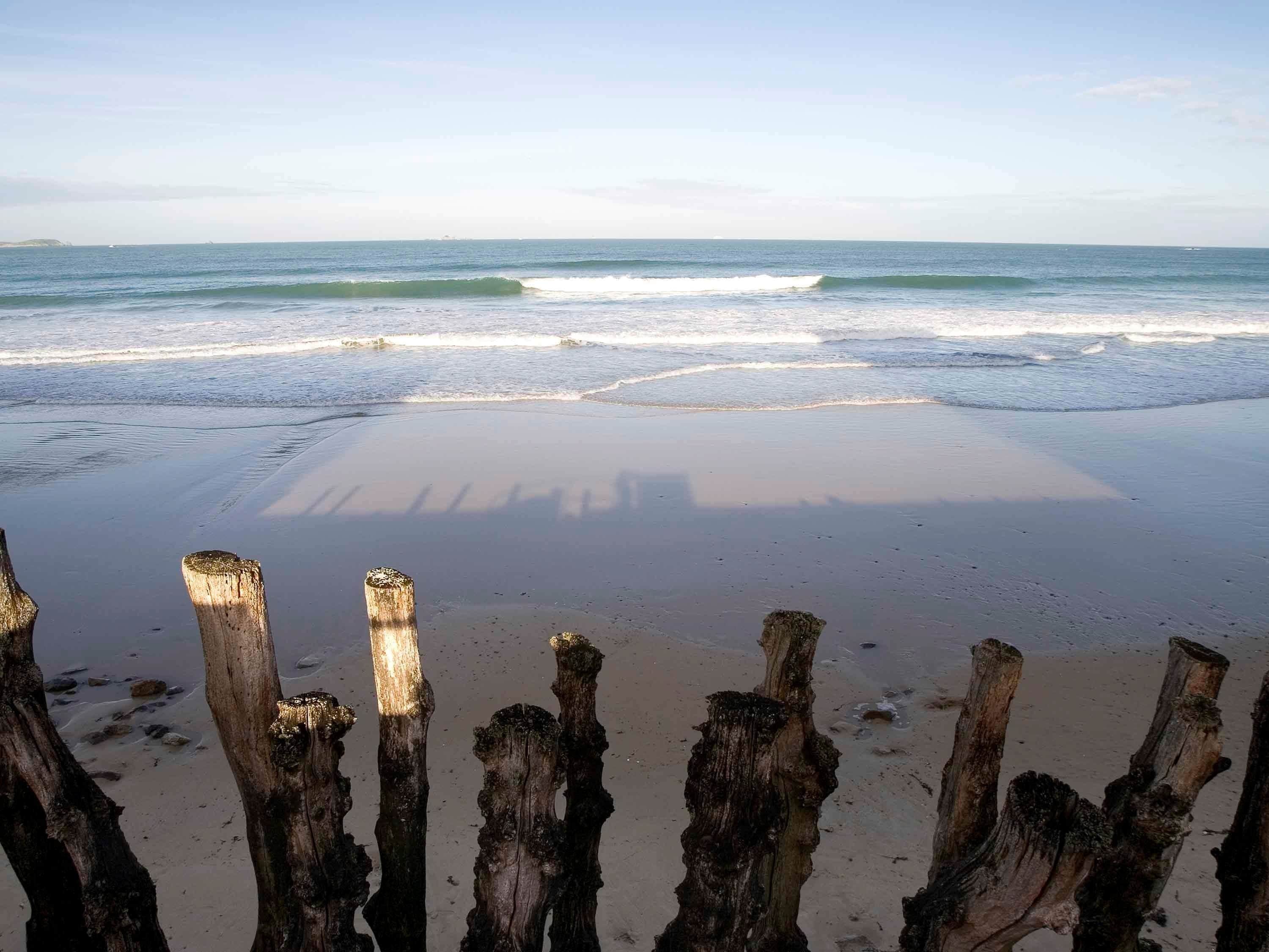 A beach with wooden posts in the foreground and waves in the background.