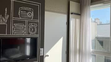 Ein Hotelzimmer mit großem Fenster, einem an der Wand befestigten Flachbildfernseher und einer Tür zu einem Balkon.