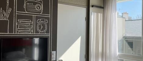 Habitación de hotel con un ventanal grande, un televisor de pantalla plana en la pared y una puerta que da a un balcón exterior.