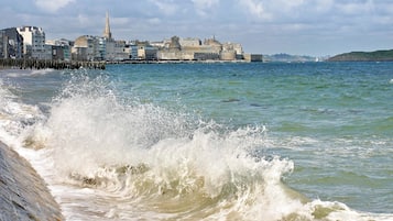 A coastal cityscape with waves crashing onto a stone pier.