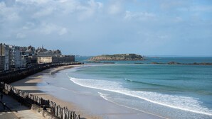 Un paysage urbain côtier avec une plage de sable, un mur de pierre et des bâtiments le long de la côte.