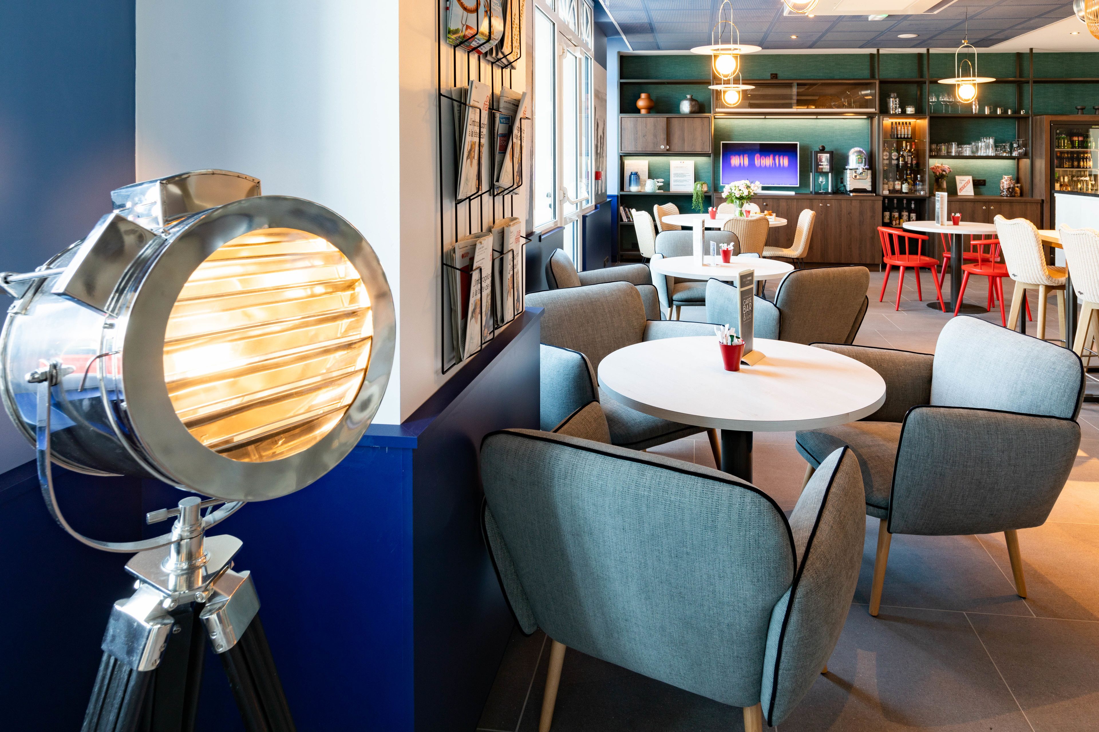 Un interior moderno con un espejo redondo, sillas tapizadas en gris, una mesa redonda blanca y una zona de bar con estanterías y una televisión.